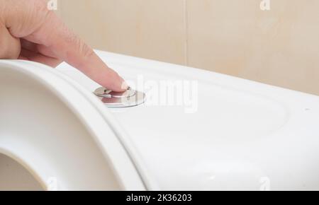 a man presses the flush button in the toilet Stock Photo