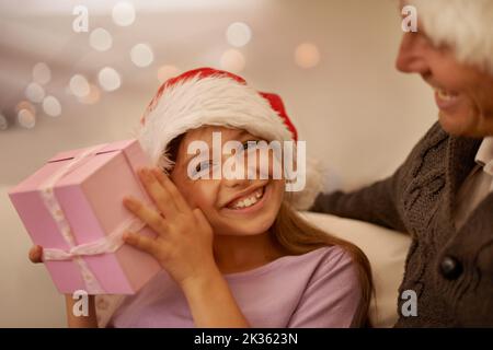 Christmas is for the kids. Smiling girl shaking her present to try and guess whats inside. Stock Photo