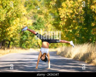 Filled with energy. A young woman doing a cartwheel in the middle of the road. Stock Photo