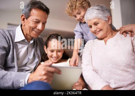 Showing granny and gramps the latest tech. A shot of two kids and their grandparents using a digital tablet while sitting on the sofa. Stock Photo