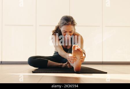 Mature woman doing a head to knee pose on a yoga mat. Senior woman doing a stretching exercise during a yoga session. Mature woman practicing a health Stock Photo