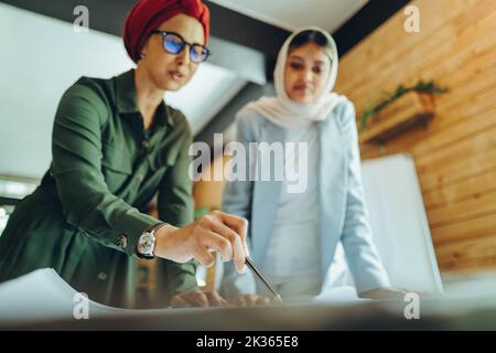Creative Muslim architects working on blueprint drawings in a modern office. Two businesswomen planning a new innovative project. Two female designers Stock Photo
