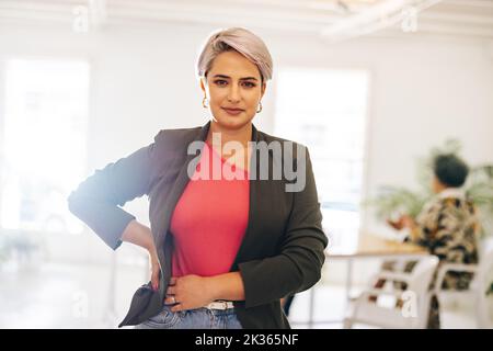 Young businesswoman looking at the camera while standing in a meeting room. Confident young businesswoman attending a meeting with her colleagues in a Stock Photo