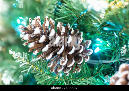 Snowy Pine Cones On Spruce Branch With Lights. Christmas or New Year blurred background with festive fir tree and pine cones. Frosty Pine Cones Hangin Stock Photo