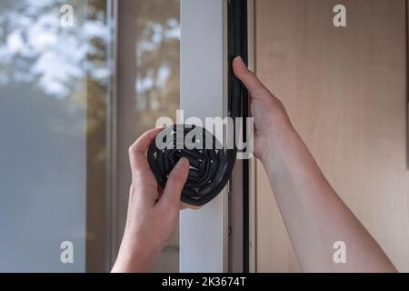 a housewife sticks a sealing rubber strip on a window. Preparing for the cold season. Stock Photo