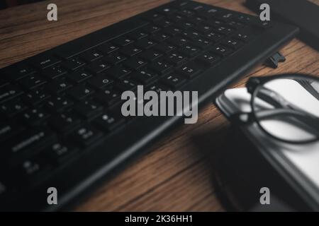 High angle view of wood vintage desk focused on keyboard with notepad and glasses. Workplace. Work from home. Office desk. Stock Photo