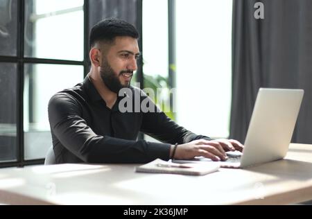 Focused young man wearing using laptop on keyboard, writing email or message Stock Photo