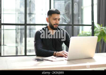 Focused young man wearing using laptop on keyboard, writing email or message Stock Photo