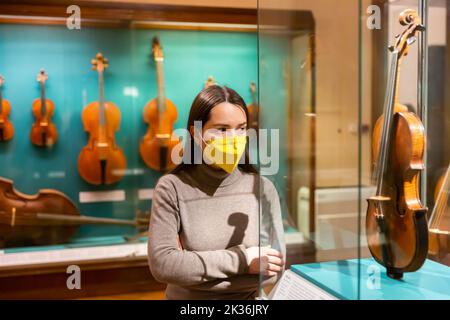 Brunette in protective mask visiting exhibition of medieval musical instruments Stock Photo