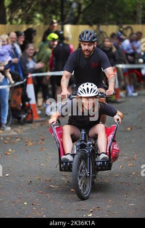 Competitors on a cargo bike racing up Swains Lane in Highgate, London during an Urban Hill Climb street racing event organised by the London Cycling Campaign, sponsored by Osbornes Law. The event is a flat-out race up the steepest street in London and alongside age and gender categories has competitions for all kinds of bike, including cargo bikes.  Swain’s Lane is the most famous and notorious climb in London. The lane is an extremely steep section of road, located in-between Hampstead Heath and Highgate Cemetery with a gradient that averages 9% over 0.6km, but increases to 14% near the top o Stock Photo