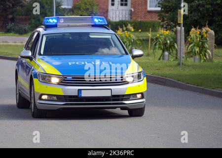 German police car on duty driving with flashing blue lights on through a rural suburb, inscription Polizei means police, copy space, selected focus Stock Photo