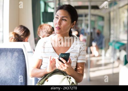 Asian woman using smartphone while sitting in tram Stock Photo
