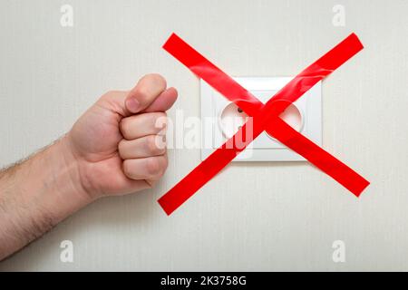 The man shows a fig gesture near the electrical outlet, tied with a red ribbon criss-cross. Stock Photo