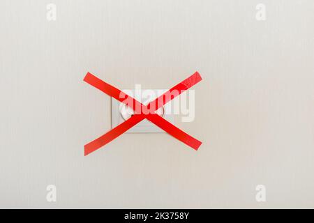 Electrical outlet, on a light wall, covered with a red ribbon cross to cross Stock Photo