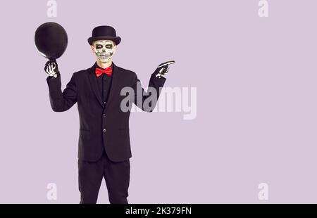 Man in skeleton Halloween costume shows something on light purple copy space background Stock Photo