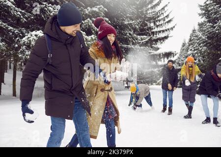 Young cheerful group of friends having fun together playing snowballs in snowy forest. Stock Photo