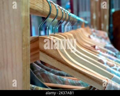 Close-up wooden clothes hangers with colorful shirts hanging on a wood cloth rack in Asian style fashion shop store. Stock Photo