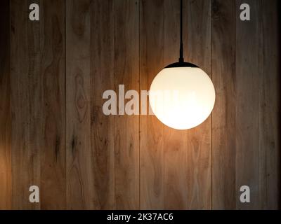 Round hanging lamp, full moon shape with the light bulb inside shining in the wood wall background in the dark room with copy space. Stock Photo