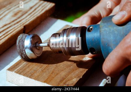 Hands man with electrical rotating brush metal disk sanding a piece of wood. Woodworking outdoors. Stock Photo