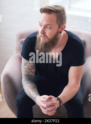 Young hipster man with beard sitting looking out window contemplating Stock Photo