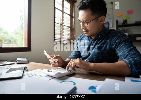 Young asian man calculating expenses household about finance and frustrated on desk at home, male checking bill having stress and worried, debt and Stock Photo