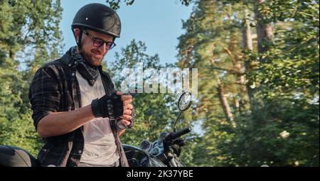 Young male biker in helmet using mobile phone and smiling sitting on a motorcycle Stock Photo