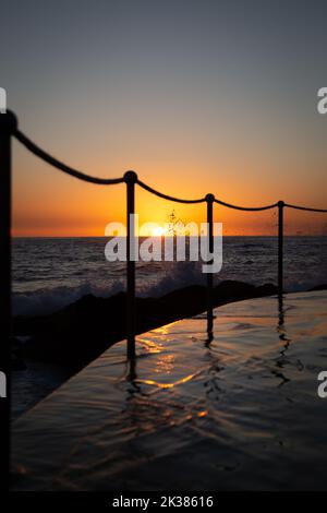 Swimming pool next to the ocean in the warm tones of sunrise in Sydney, New South Wales, Australia Stock Photo