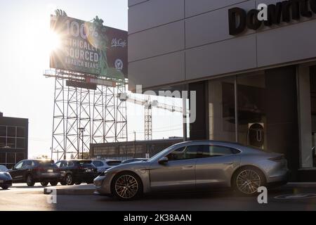 A silver Porsche Taycan, the automaker's first electric vehicle sits out front of a Porsche dealer in downtown Toronto as the morning sun shines down. Stock Photo
