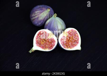 Ripe figs, half cut and whole fruits on dark wooden table Stock Photo