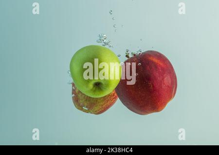 Close up view of red and green apples falling into water isolated on turquoise water background. Stock Photo