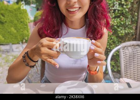 The girl smiles with snow-white teeth and drinks cappuccino coffee in a cafe Stock Photo