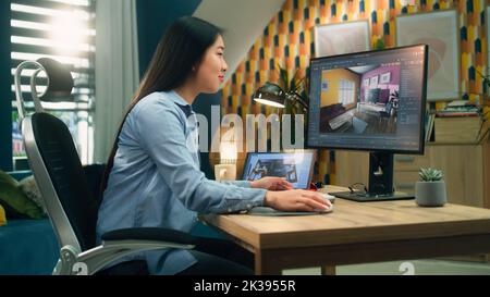 Female asian designer working remotely from home office and making 3D visualization of house interior in computer program using pc and digital tablet Stock Photo