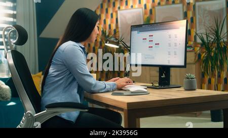 Female asian web designer using personal computer for creating website in professional constructor while working on project remotely at home. Freelance Stock Photo