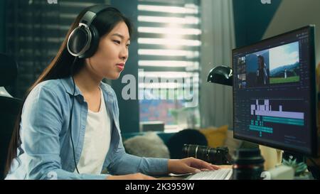 Female asian freelancer editing video for customer or travel blogger in program on computer while sitting at the table and working at home Stock Photo
