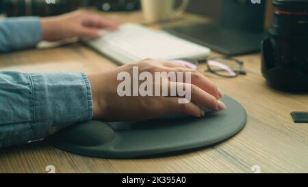 Close-up of hand of woman or female freelancer using computer mouse and clicking, while surfing the internet in spare time or working remotely from home. Stock Photo
