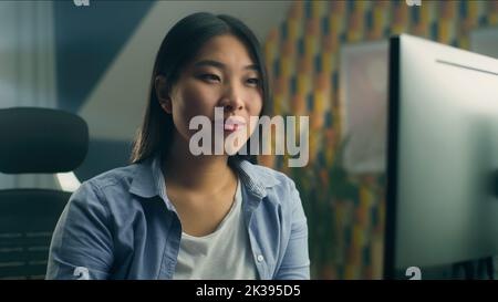Asian woman sitting at the table at home office and working remotely on personal computer or browsing the internet in spare time Stock Photo