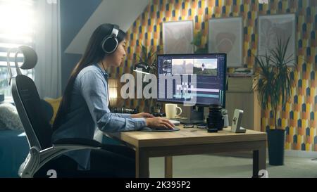 Asian woman sitting at the desk in headphones at home office and editing video for blog in professional program on computer. Freelance Stock Photo