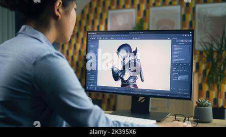 Female 3D designer creating and drawing character for video game using computer while sitting at the table at home office and doing distant work. 3D modeling Stock Photo