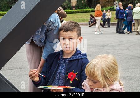 Dnipro, Ukraine - September 10, 2022: Boy artist paint metal anti-tank obstacle czech hedgehog in front-line city during the russian-Ukrainian war of Stock Photo