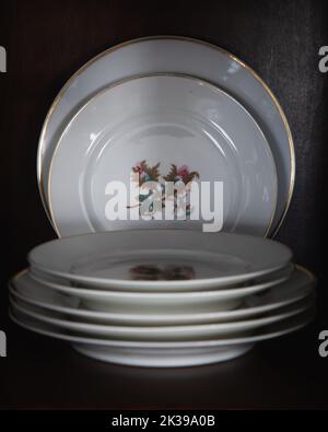 Porcelain Dinner and Dessert Plates with Flower Detail and Gold Trip Stacked and Displayed in a China Cabinet Stock Photo