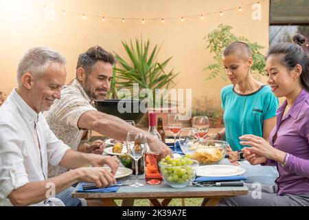 Multiracial friends laughing around the diner table. Together enjoying life concept. Stock Photo
