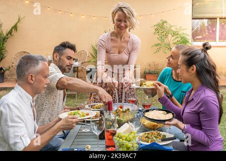 Multiethnic mature friends eating enjoying happy smiling and laughing in the backyard at home togetherness. Stock Photo