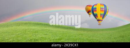 Hot Air Baloons Drift Above Grass Field with Rainbow in the Sky. Stock Photo
