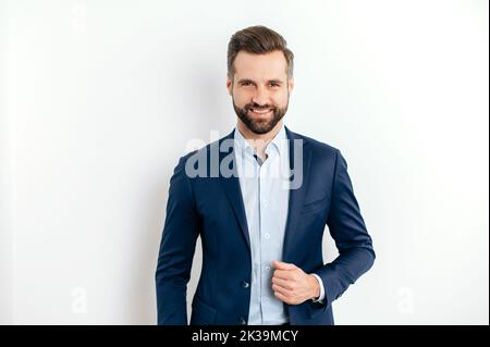 Portrait of a proud confident handsome bearded caucasian businessman, successful ceo, in formal elegant suit, standing on isolated white background, looking at the camera, smiling friendly Stock Photo