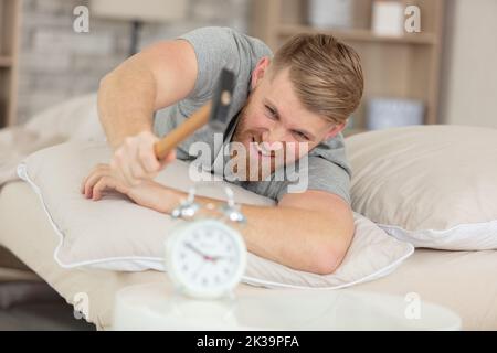 young man tries to break the alarm clock with hammer Stock Photo