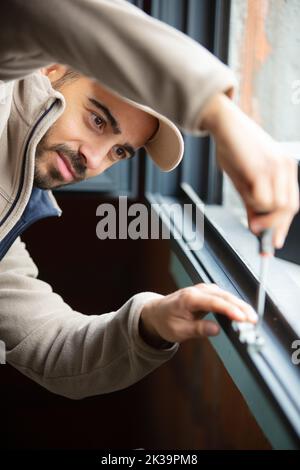 construction worker repairing plastic window with screwdriver indoors Stock Photo