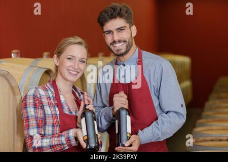 two friendly smiling winemakers in uniform examining bottle of wine Stock Photo