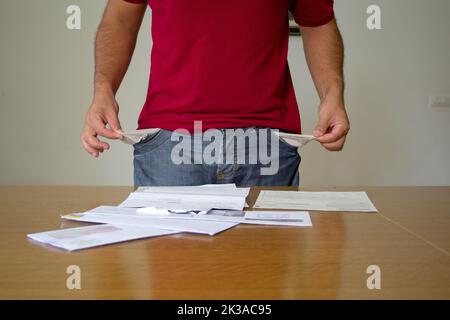 man with his trouser pockets turned inside out in front of some electricity and gas bills. increase in the cost of bills due to the global crisis Stock Photo
