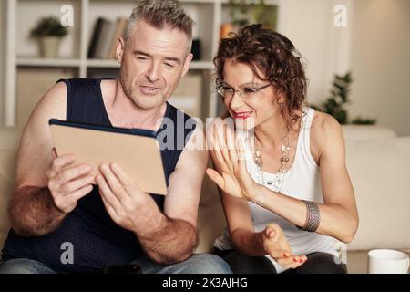 Happy stylish mature couple using tablet computer when video calling friends Stock Photo