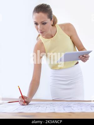 Making sure the blueprints are in order. An attractive young woman working on a blueprint. Stock Photo